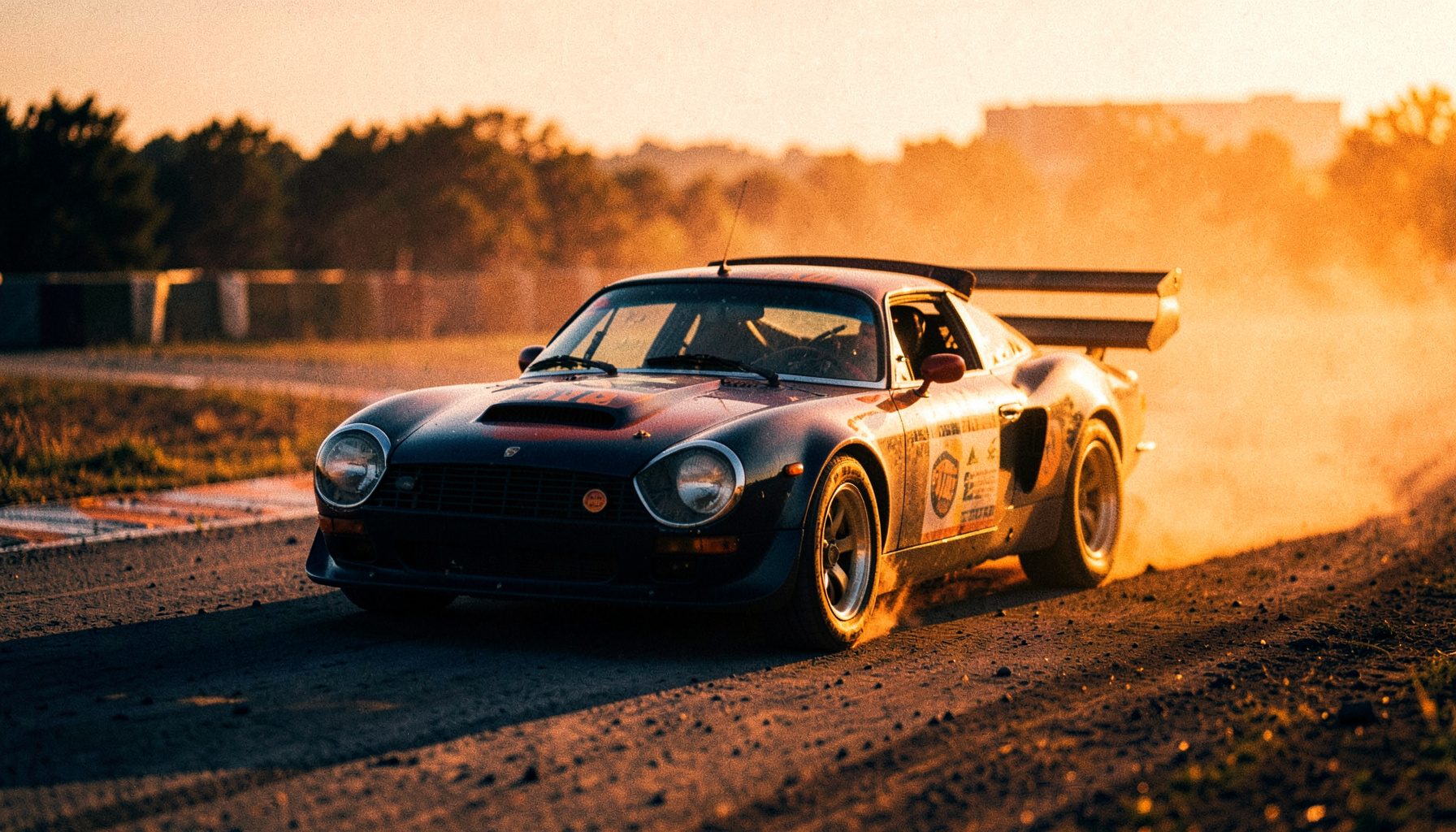 Historisches Rennauto auf einer staubigen Rennstrecke in der Abenddämmerung, warmes goldenes Licht, dunkelblaue und orange Akzente