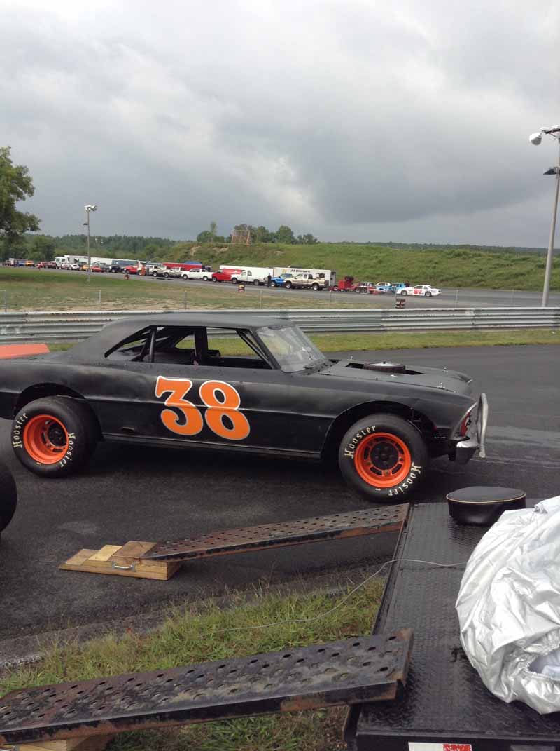 Historischer Rennwagen mit orangefarbener Startnummer auf der Seite, geparkt auf einer Rasenfläche an der Rennstrecke